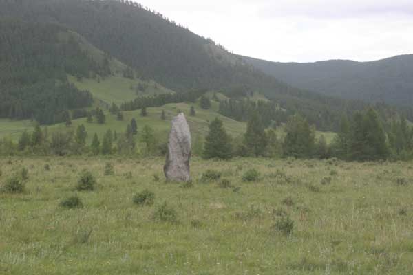A single standing stone with mountains and forest in the background