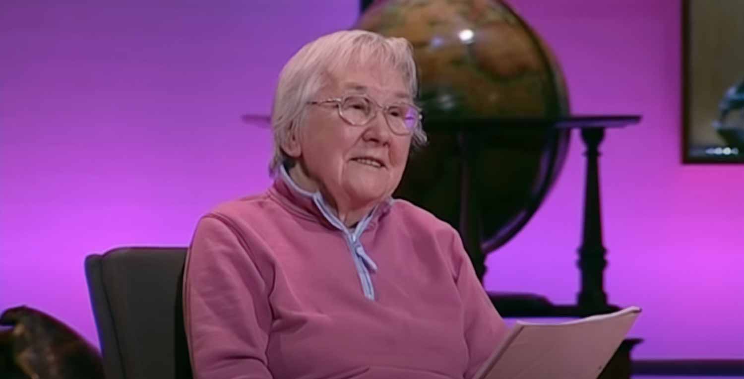 Elaine Morgan seated in front of an antique globe, with a bright purple background