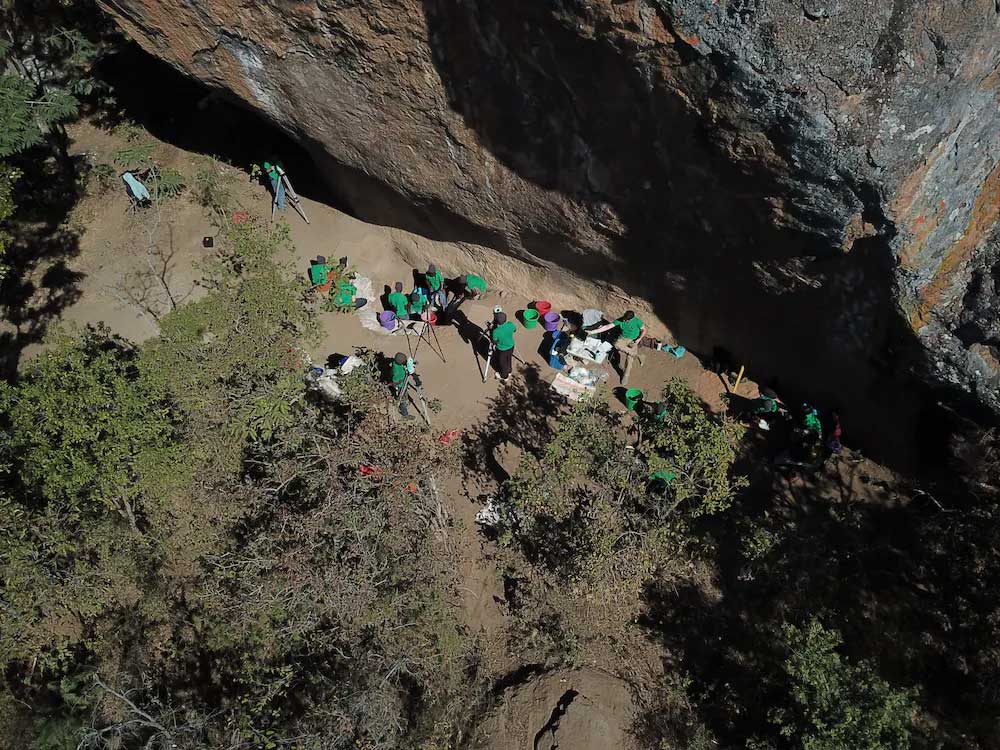 An overhead view of archaeologists working next to a high cliff face