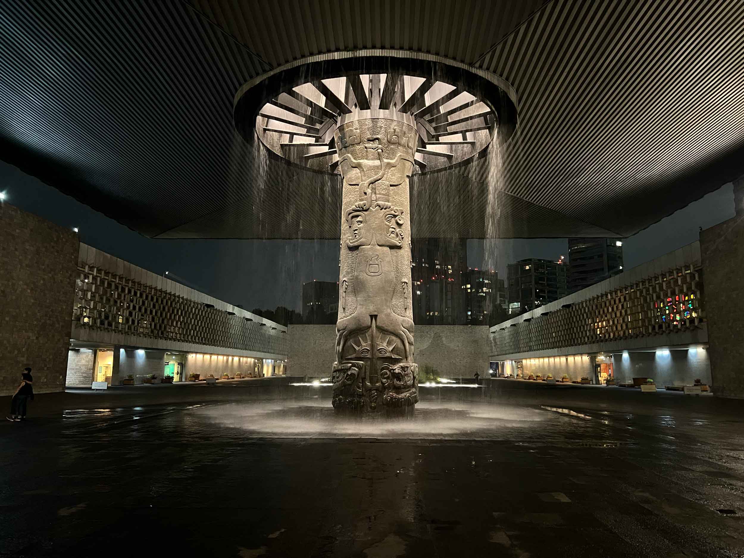 An elaborate column holding up a large roof over a courtyard, with water streaming from a circular hole around the column.