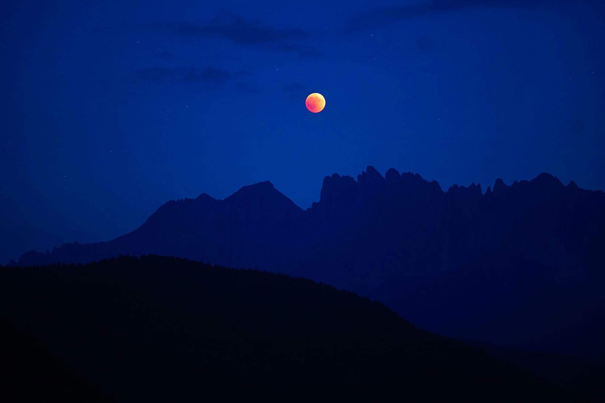 Lunar eclipse showing red moon on purple sky background with dramatic jutting mountain range silhouetted beneath